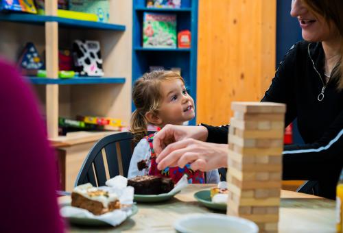 Little girl sat at a table with cake and Jenga game